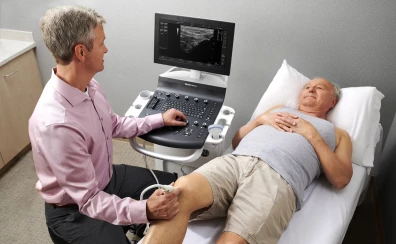Lekarz wykonuje badanie USG kolana pacjentowi leżącemu, aparatem Versana Balance