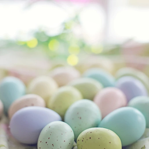 Dużo kolorwych jajek w pastelowych kolorach, niektóre z brązowymi plamkami. Jajka leżące w oddali są rozmazane.